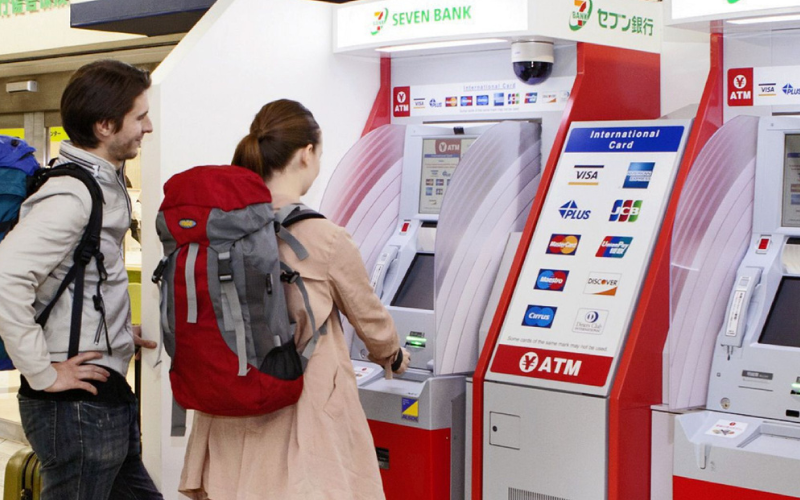 Turisti che usano un bancomat Seven Bank in Giappone per prelevare con carte internazionali