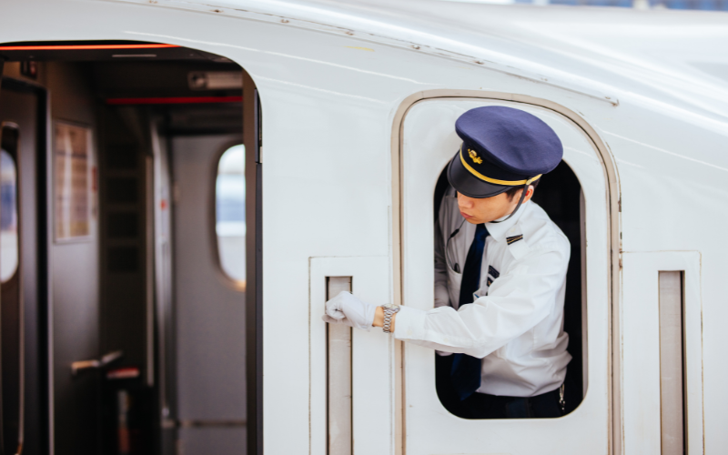 Capotreno giapponese affacciato dal finestrino dello Shinkansen durante il controllo prima della partenza